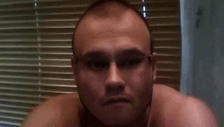 a man without a shirt is looking at the camera in front of blinds