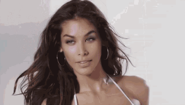 a woman wearing hoop earrings and a white bikini top looks at the camera