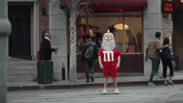 a man in a santa costume with the letter m on his shirt is crossing a street