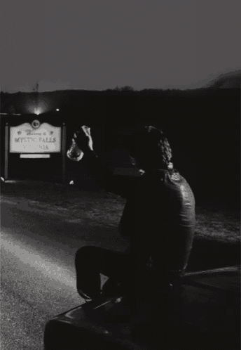 a man is sitting in front of a mystic falls virginia sign