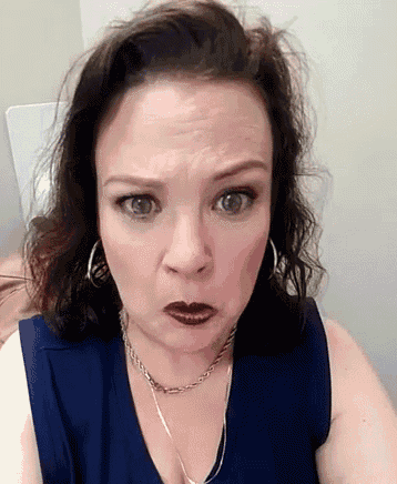 a woman wearing a blue shirt and a necklace is making a funny face