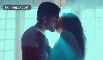 a man and woman are kissing in front of a window in a room .