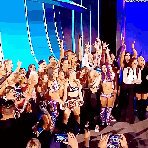 a group of women are posing for a picture on a stage with their hands in the air .