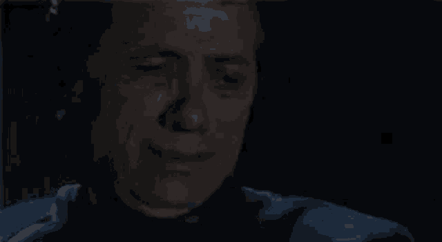 a man is crying with his eyes closed in a dark room .