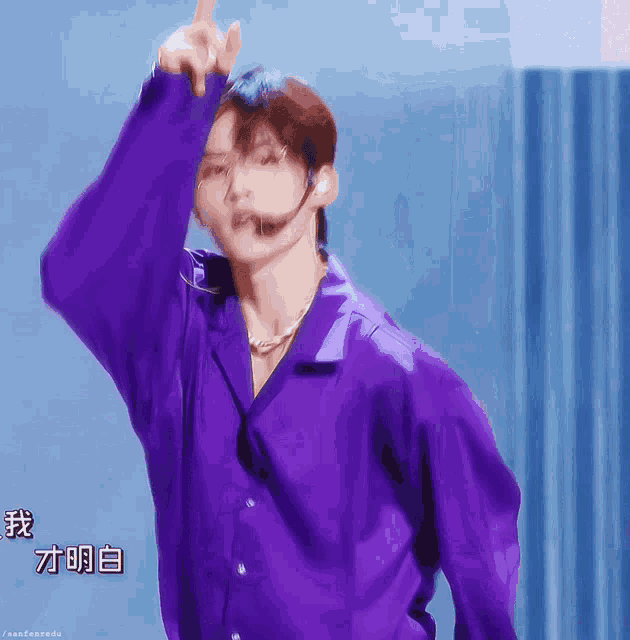 a man in a purple shirt is pointing up with chinese writing behind him