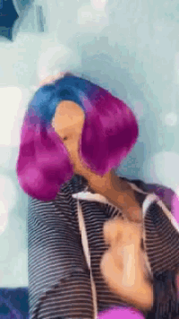 a woman with purple and blue hair is wearing a striped hoodie