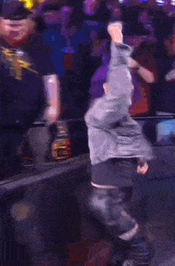 a woman with purple hair is dancing in front of a crowd in a dark room .