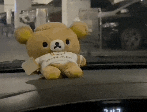 a teddy bear is sitting on the dashboard of a car with a t-shirt on