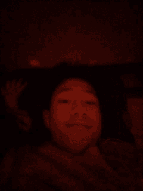 a man in a dark room with a hand behind his head