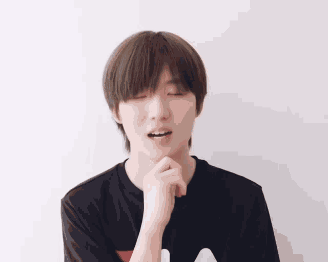 a young man with his eyes closed and his hand on his chin is wearing a fila shirt