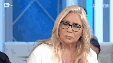a woman wearing glasses and a white shirt is sitting on a couch on a television show .