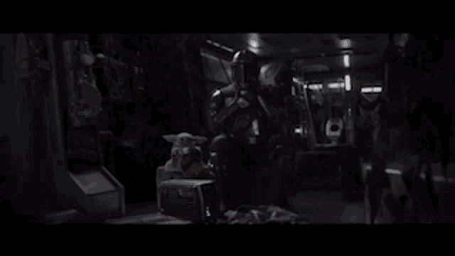 a group of people are standing in a dark room with a baby yoda sitting on the floor .