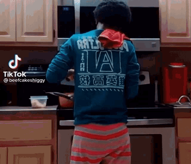 a man in a blue shirt is cooking in a kitchen with a red towel on his shoulder .
