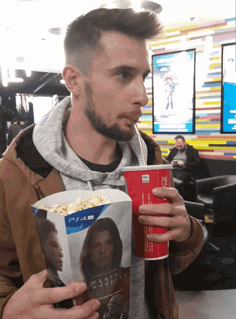 a man drinking from a coca cola cup while holding popcorn
