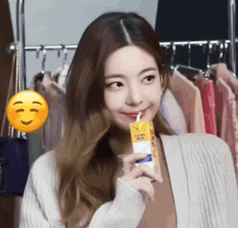 a woman is drinking from a carton with a straw while wearing a sweater .