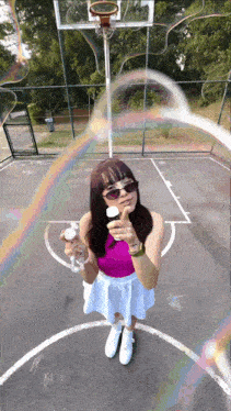 a woman blowing soap bubbles on a basketball court with a rainbow in the background