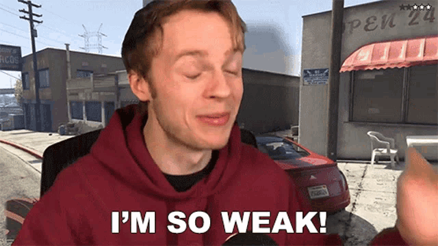a man in a red hoodie says " i 'm so weak " in front of a red car