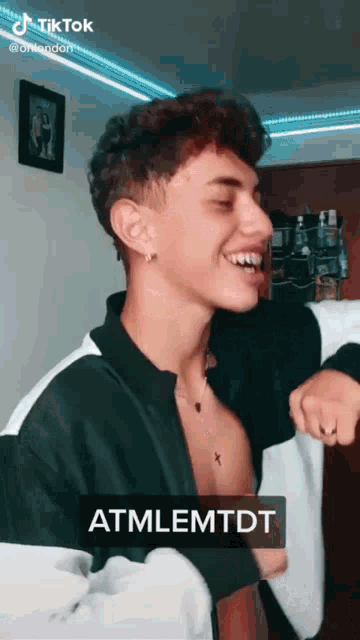 a young man in a black and white jacket is laughing with a caption that reads atmlemtdt
