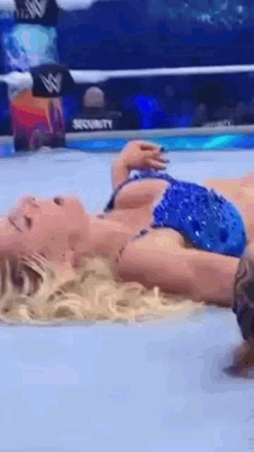 a woman in a bikini is laying on the floor in a wrestling ring .