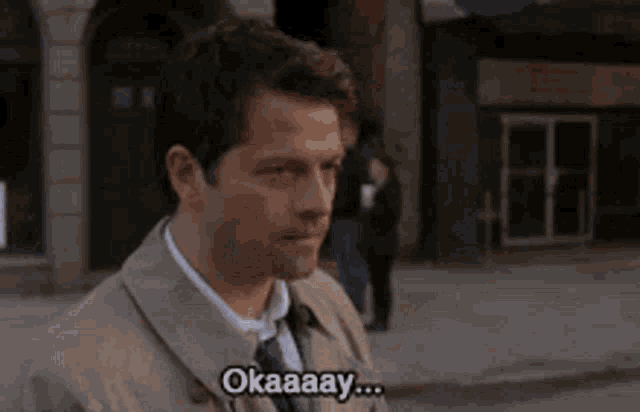 a man in a suit and tie is standing in front of a building and saying okaaay .