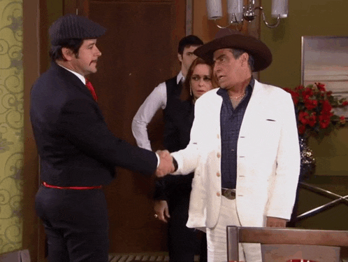 a man in a white suit shakes hands with another man in a cowboy hat