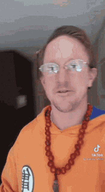 a man wearing glasses and a necklace is wearing an orange hoodie .