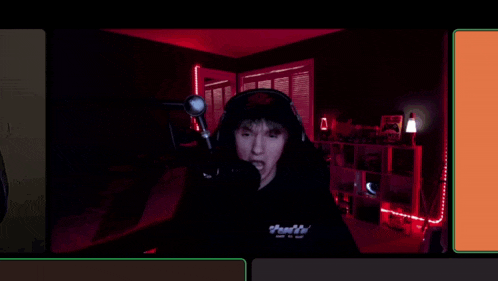 a man wearing headphones and a hoodie is sitting in front of a microphone .