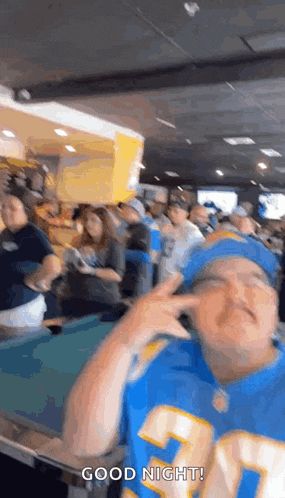 a man in a la chargers jersey is standing in front of a pool table and making a funny face .