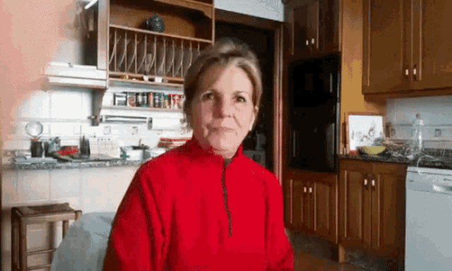 a woman wearing a red sweater is sitting in a kitchen