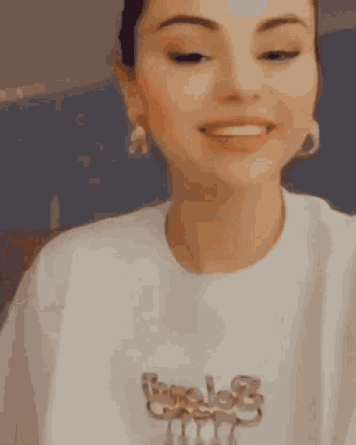 a woman wearing a white t-shirt and earrings is smiling .