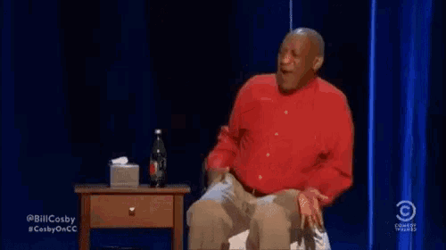 a man in a red shirt is sitting on a table with a bottle of diet coke on it .