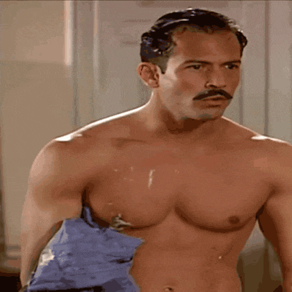 a shirtless man with a mustache is talking to another man