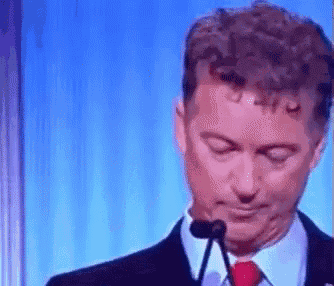 a man in a suit and tie is speaking into a microphone with his eyes closed