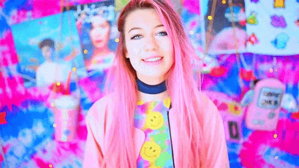 a woman with pink hair is smiling in front of a colorful wall .