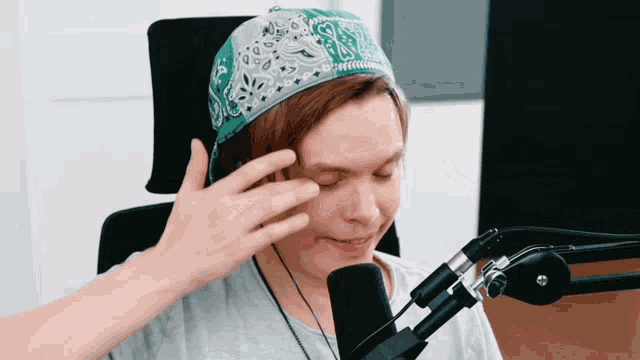 a man wearing a bandana is sitting in front of a microphone and touching his forehead