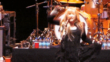 a woman singing into a microphone on a stage in front of a drum set