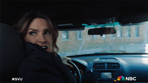 a woman is driving a car with nbc written on the dashboard