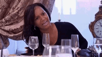 a woman is sitting at a table with wine glasses and a clock on it .