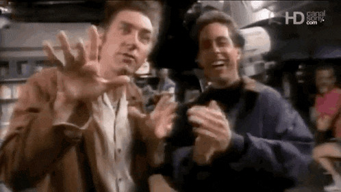 two men are standing next to each other and clapping their hands in a room .