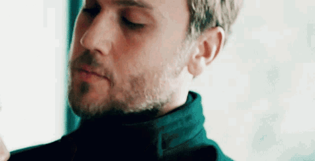 a close up of a man with a beard wearing a black turtleneck sweater