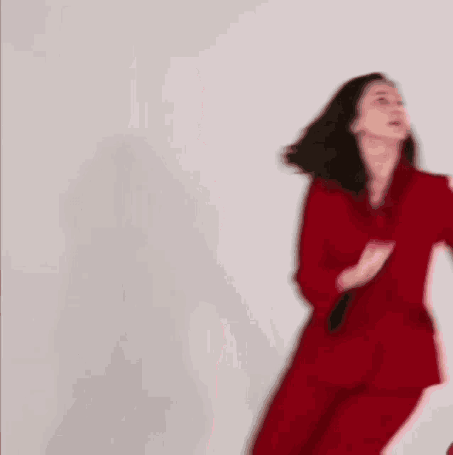 a woman in a red suit is standing in front of a white wall and dancing .