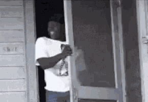 a man is standing in the doorway of a building holding a bottle of beer .