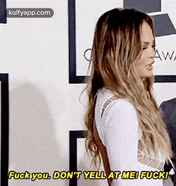 a woman with long hair is standing in front of a wall and yelling at someone .