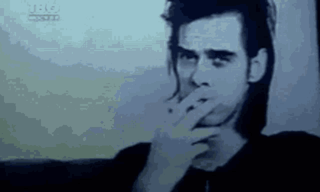 a man is smoking a cigarette and covering his mouth with his hand .