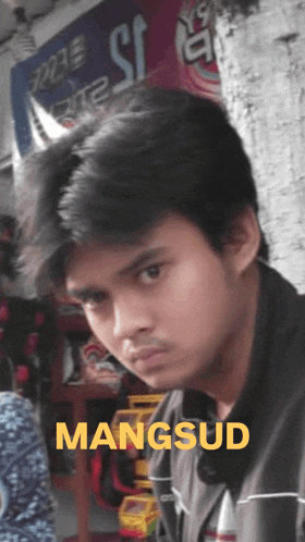 a young man stands in front of a sign that says mangsud on it