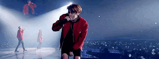 a man in a red jacket is holding a microphone on a stage .