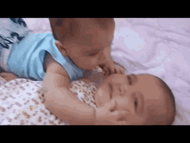 two babies are laying on a bed and one is kissing the other 's face .