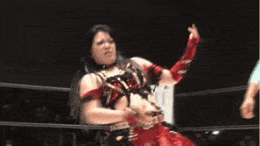 a woman in a red and black outfit is standing in a wrestling ring