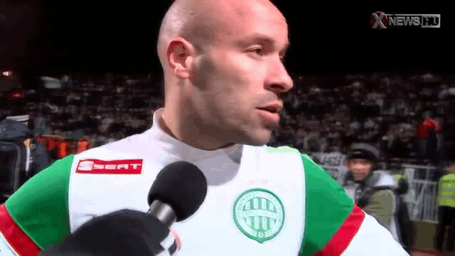 a bald man wearing a seat shirt is talking into a microphone