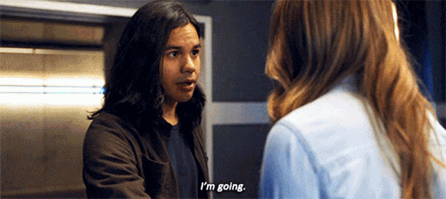 a man with long hair is talking to a woman and says i 'm going